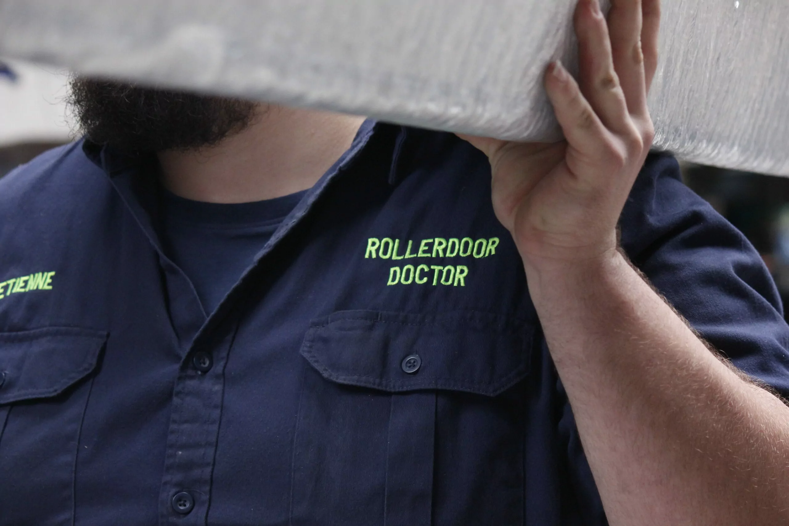 Image of man wear a rollerdoor doctor shirt while lifting a piece of equipment.